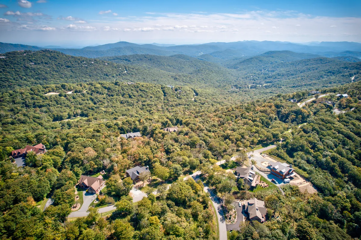 A sweeping view of verdant forests, rolling mountains in the distance, scattered homes, and winding roads. The landscape is alive with lush greenery, hinting at local hiking trails, wildlife exploration, and sunset vistas that define the area's outdoor adventure appeal.