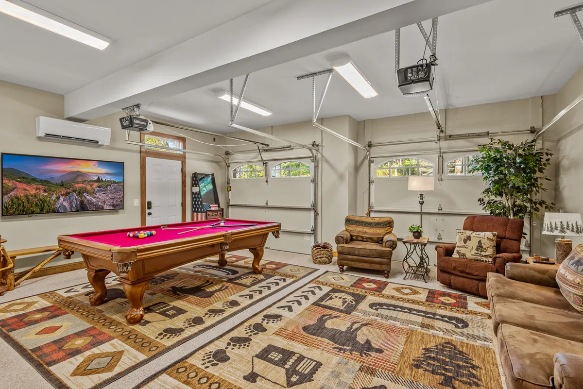 A spacious entertainment lounge with a pool table in the foreground, a large television against the wall, and plush, inviting seating. The decorative rug adds warmth and character, while the overall setup suggests a perfect environment for both gaming and movie nights.