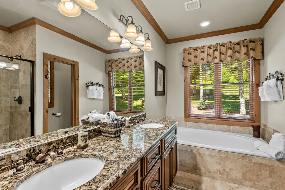 A spacious bathroom with granite double sinks, a large bathtub, open shower area, and a window bringing in natural light. The calming and functional design offers a true retreat for daily routines or unwinding after mountain adventures.