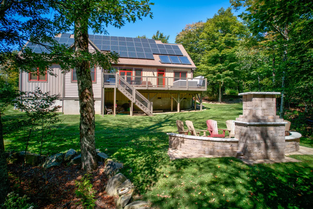 This image highlights the expansive deck area, complete with solar panels, a fire pit, lawn, and surrounding trees. The scene suggests space for outdoor gatherings, evening fireside conversations, and family barbecues, extending group entertainment beyond the interior.