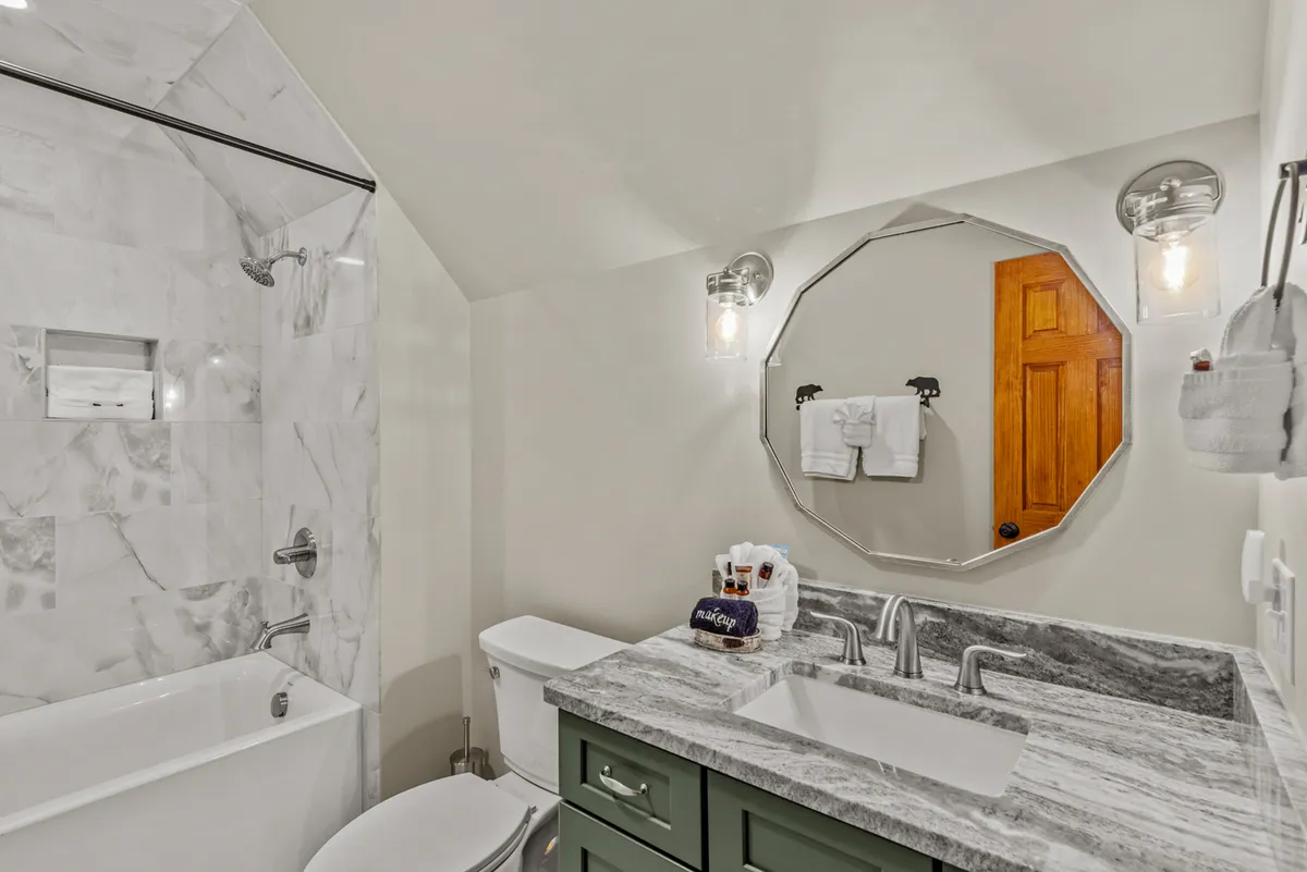 A spa-inspired bathroom with a marble shower, octagonal mirror above a stylish vanity, and calming green cabinetry. The space feels modern, clean, and designed for rejuvenation.