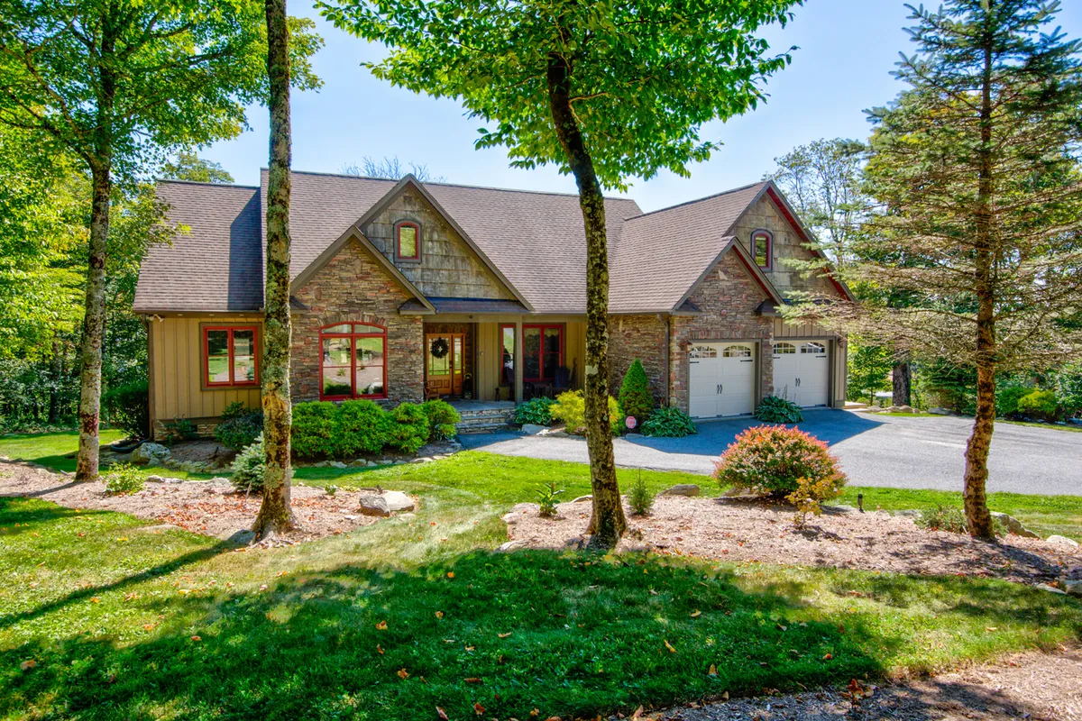 This exterior shot showcases The Trinity's stone facade, lush green lawn, and spacious front porch. The inviting outdoor space hints at group relaxation and social opportunities before heading indoors for entertainment.