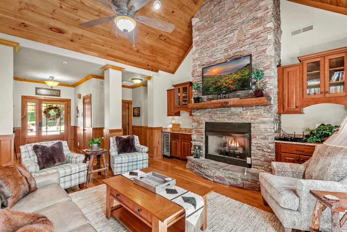 A cozy interior scene with a prominent stone fireplace, high wooden ceiling, and comfortable seating arranged for warmth and conversation. The inviting ambiance is perfect for watching the snowfall or warming up after winter adventures.