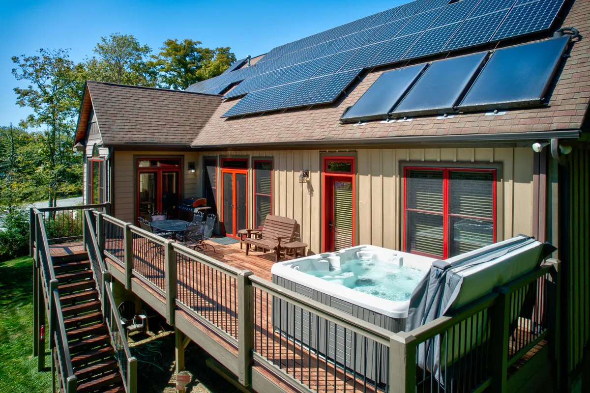 This image highlights the outdoor deck area featuring a spacious hot tub, solar panels on the roof, and ample outdoor seating surrounded by trees. The setting is tranquil and inviting, suggesting relaxation after a day on the slopes.