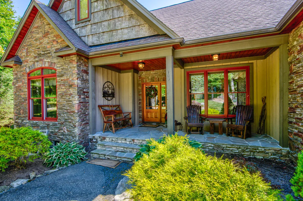 The image showcases the inviting stone facade of the mountain home, accented by vibrant red window frames and a welcoming front porch lined with classic rocking chairs. The scene evokes a sense of warmth and togetherness, suggesting a perfect spot to relax, watch sunsets, and share stories with friends and family.